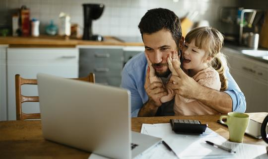 Happy parent playing with child while still being able to research into the correct insurance he needs. 